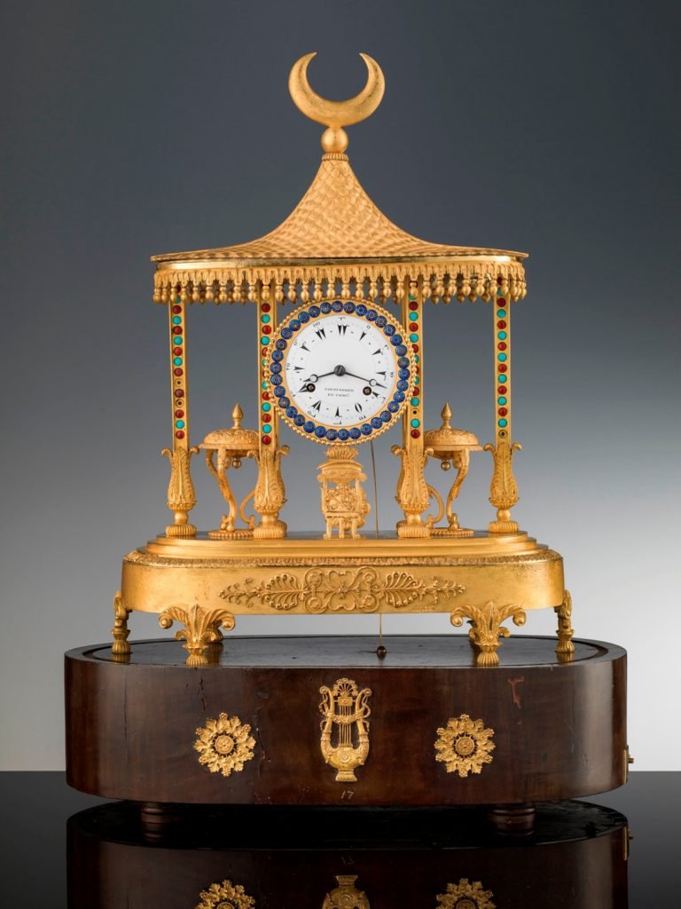 Reloj de sobremesa de Louis Courvoisier y Compañía, 1811-14, bronce dorado y esmalte policromado, en base de chapa de madera y bronce dorado, 57 × 42 × 23 cm, Florencia, Galería de los Uffizi, Galería de Arte Moderno del Palazzo Pitti.