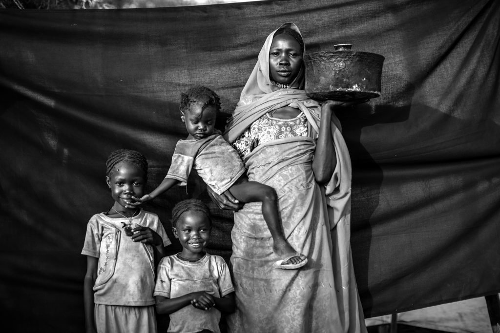 Magboola, 20 años, en el campamento de refugiados de Jamam, Maban, Sudán del Sur. Ella y su familia resistieron varios ataques aéreos durante meses, pero decidieron huir de su pueblo, Bofe, la noche en que los soldados se presentaron en él abriendo fuego. Junto con sus tres hijas, viajó durante doce días desde Bofe, en el estado sudanés de Nilo Azul, hasta la localidad de El Fudj, en la frontera de Sudán del Sur. Lo más importante que se llevó consigo es la olla que sostiene en esta fotografía, lo suficientemente pequeña como para poder viajar con ella y lo suficientemente grande como para cocinar el sorgo para ella y sus tres hijas durante el viaje.